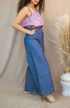 a woman standing next to a tall plant wearing blue pants and a tank top with pink tie dye