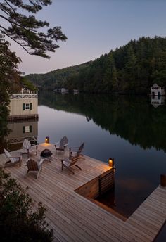 a dock with chairs and lights on it next to a body of water at dusk