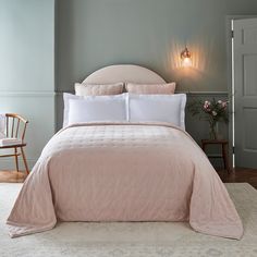 the bed is made up with pink sheets and white comforter, along with two wooden chairs