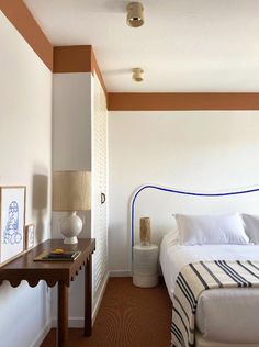 a white bed sitting next to a wooden table with a lamp on top of it