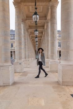 a woman in black boots and a hat is walking down the street with columns on both sides