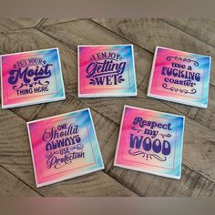 four stickers with different sayings on them sitting on a wooden surface, one is pink and the other is blue