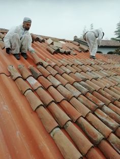 two men working on the roof of an old building with clay tiles and shingles