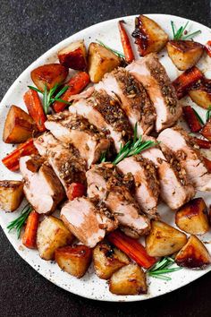 a white plate topped with sliced pork and potatoes on top of a black countertop