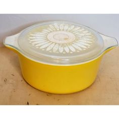 a yellow casserole dish with a glass lid on a wooden tablecloth covered surface