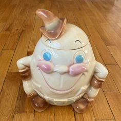 a ceramic toy with a smiling face on it's head sitting on a wooden floor