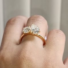 a woman's hand holding a gold ring with two diamonds on top of it