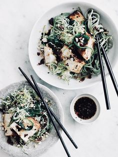 two plates of food with chopsticks next to each other on a white table