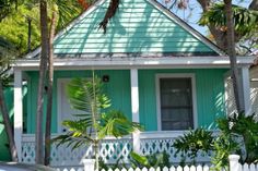 a blue house with white picket fence and palm trees