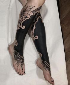 a woman's legs with tattoos on them sitting on a white sheet in front of a wooden floor