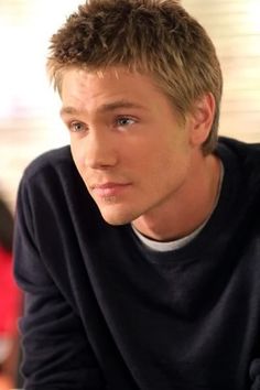 a young man sitting at a table with his hand on his chin and looking off to the side