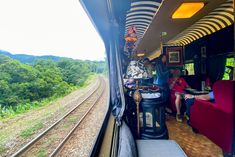 people sitting on the inside of a train looking out the window at trees and mountains