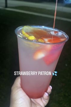 a hand holding a drink with strawberries in it