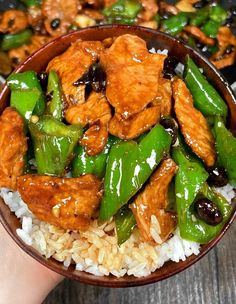 a person holding a bowl filled with chicken and snow peas on top of white rice