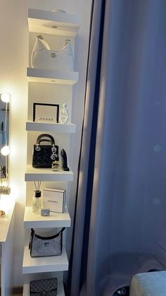 a white shelf filled with purses next to a bathroom sink and shower curtain in front of a mirror