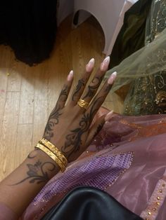 a woman's hands with tattoos and gold bracelets on her left hand, sitting on the floor