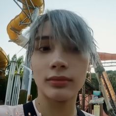 a young man with grey hair standing in front of a roller coaster