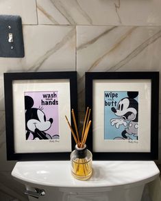 two framed mickey mouse pictures next to a toothbrush holder with reeds in it