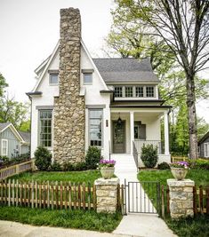 a small white house with a stone chimney and picket fence in front of the door