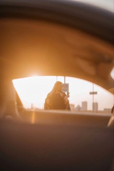 a woman standing in the back seat of a car looking at her cell phone as the sun is setting