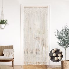 a living room with white walls and wooden flooring next to a window covered in macrami curtains