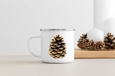 a white coffee mug sitting on top of a wooden table next to two pine cones