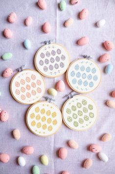 four cross stitch easter egg designs on a table with pastel colored eggs around them