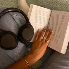 a woman reading a book with headphones on her lap and holding an open book