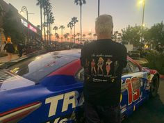 a man standing next to a race car on the side of a road at sunset