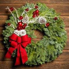 a christmas wreath with pine cones and red ornaments on a wooden background, top view