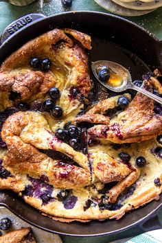 a pan filled with blueberries and chicken on top of a green table cloth next to utensils