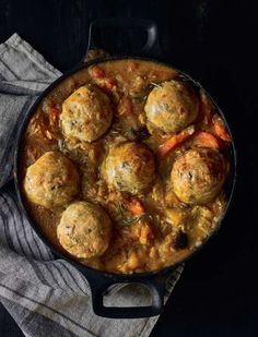 a pot filled with meatballs and vegetables on top of a cloth next to a fork