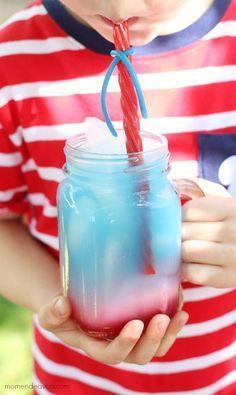 a young boy holding a blue and red drink in his hand with a straw sticking out of it