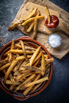 french fries in a bowl with ketchup and dipping sauces on the side