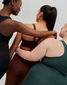 three women in sports bras are looking at each other while one woman is holding her arm around the other