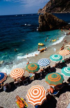 many umbrellas are set up on the beach by the water's edge as people swim in the ocean