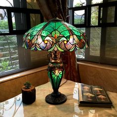 a green lamp sitting on top of a table next to a book and potted plant