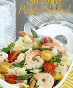 shrimp pasta salad in a white bowl with lemons and tomatoes