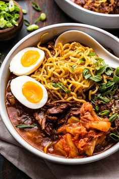 two bowls filled with noodles, meat and eggs on top of a table next to other dishes