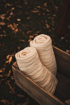 two pairs of white socks sitting in a wooden box on the ground next to fallen leaves