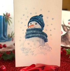 a card with a snowman wearing a blue knitted hat and scarf on it