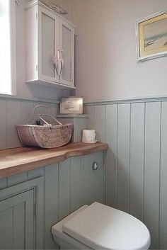 a white toilet sitting in a bathroom next to a sink under a window on top of a wooden counter