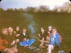 a group of people sitting on top of a grass covered field next to each other