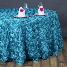 two wine glasses sitting on top of a table covered with a blue cloth and red flower