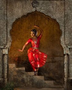 a woman in a red and gold dress dancing on steps with her arms raised up