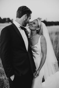 a bride and groom standing in the middle of a field with tall grass behind them