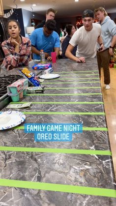 a group of people standing around a table with food on it and the words family game night oreo slide