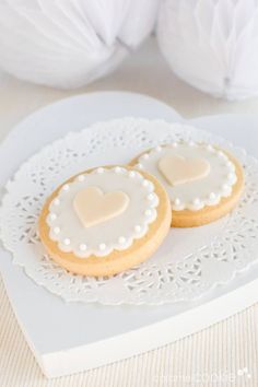 two heart shaped cookies sitting on top of a white doily next to paper flowers