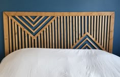 a bed with white sheets and wooden headboard against a blue wall in a bedroom