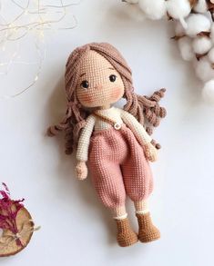 a crocheted doll laying on top of a white table next to some flowers